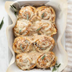 Butternut squash rolls in a baking dish topped with fresh sage.
