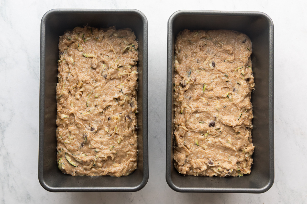 Two loaf pans filled with zucchini bread batter.