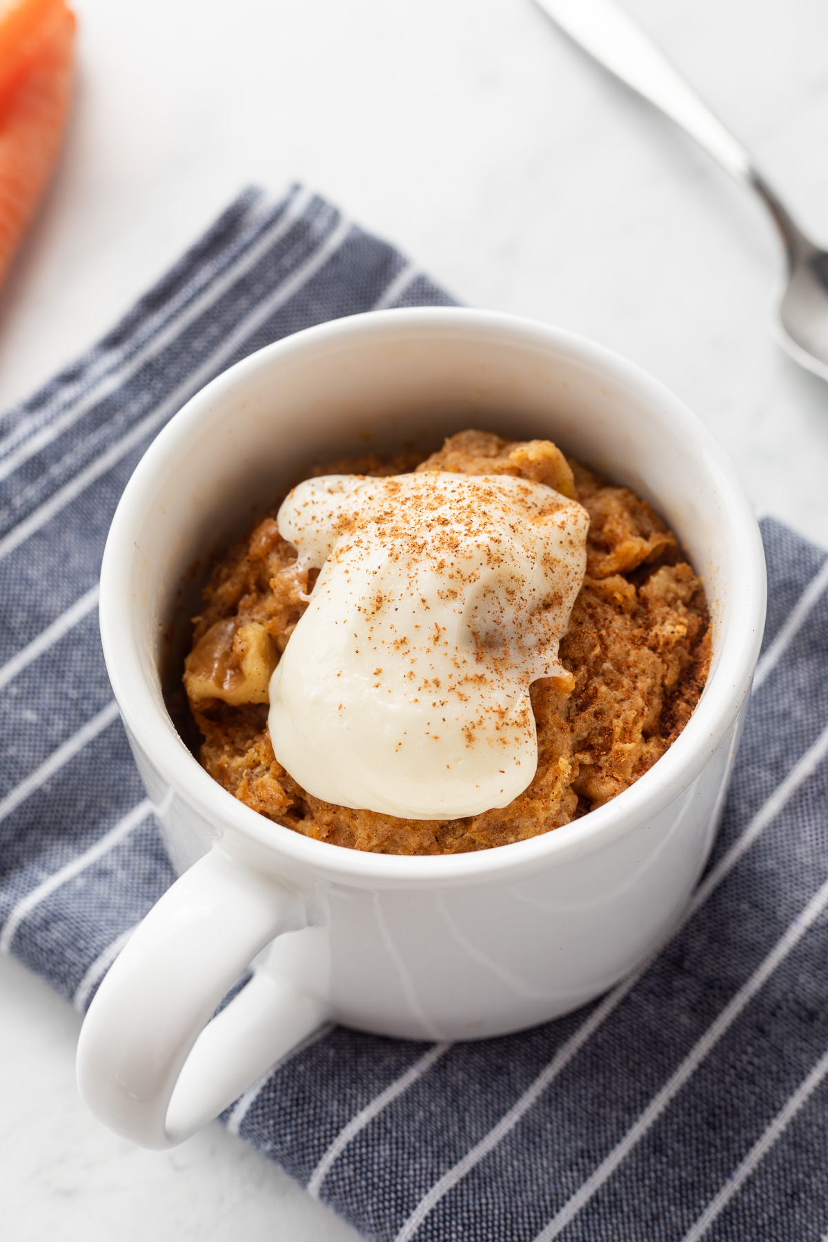 Carrot cake mug cake in a white mug topped with whipped cream cheese frosting.