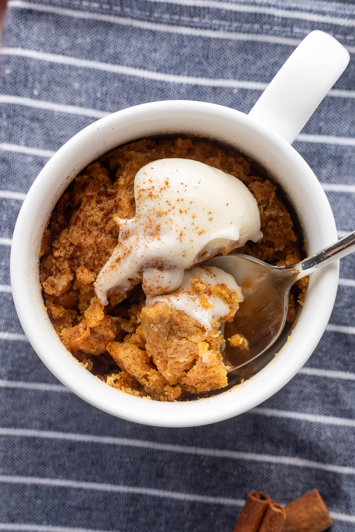 Carrot cake mug cake in a white mug topped with whipped cream cheese frosting with a spoon digging into it.
