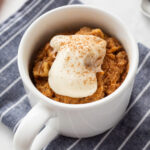 Carrot cake mug cake in a white mug topped with whipped cream cheese frosting.