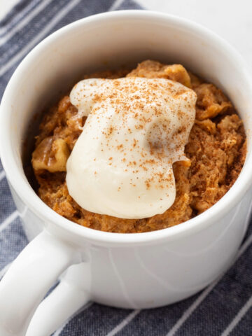 Carrot cake mug cake in a white mug topped with whipped cream cheese frosting.
