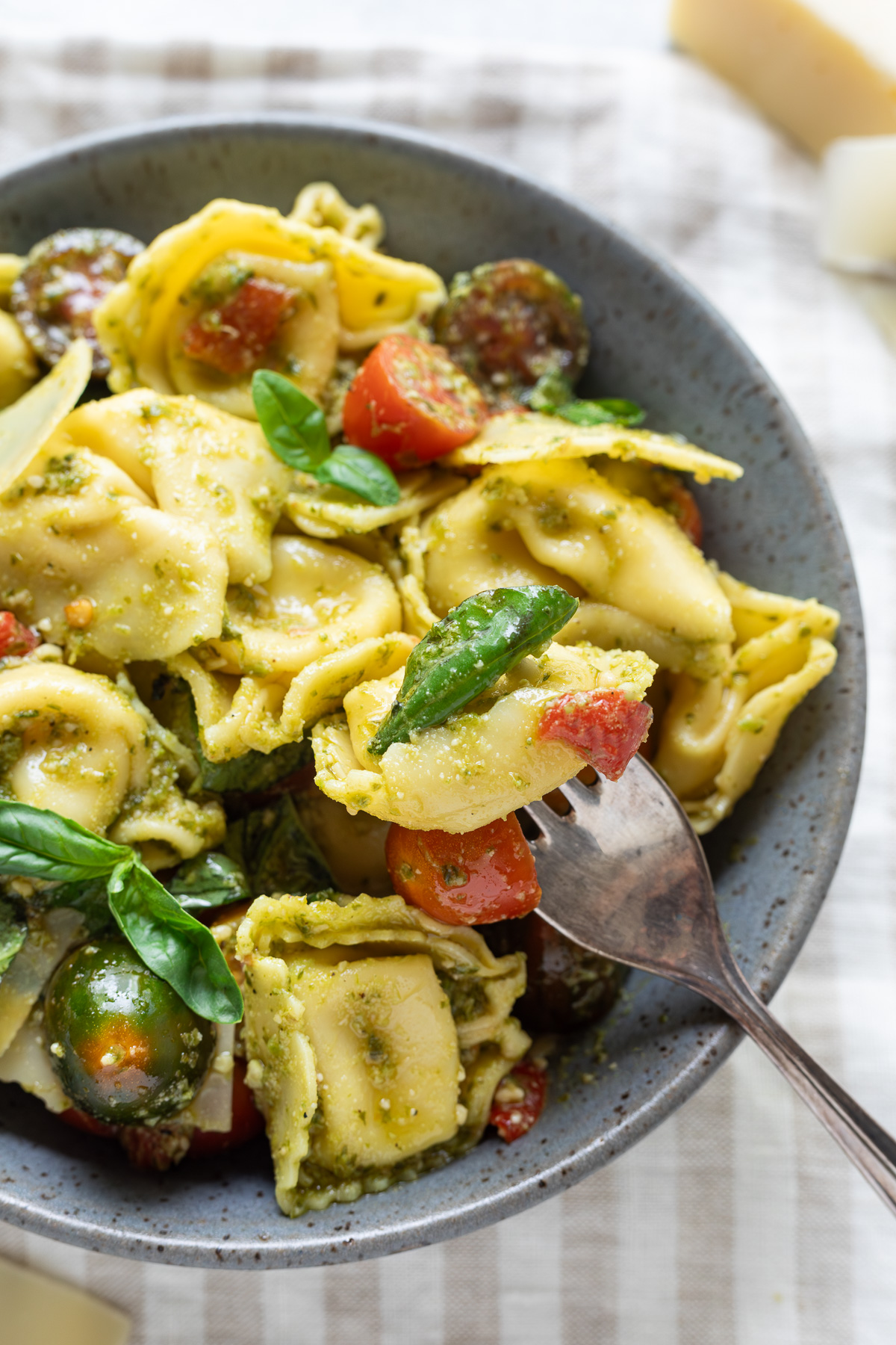 Pesto tortellini salad in a bowl with a fork stuck in one of the tortellini.