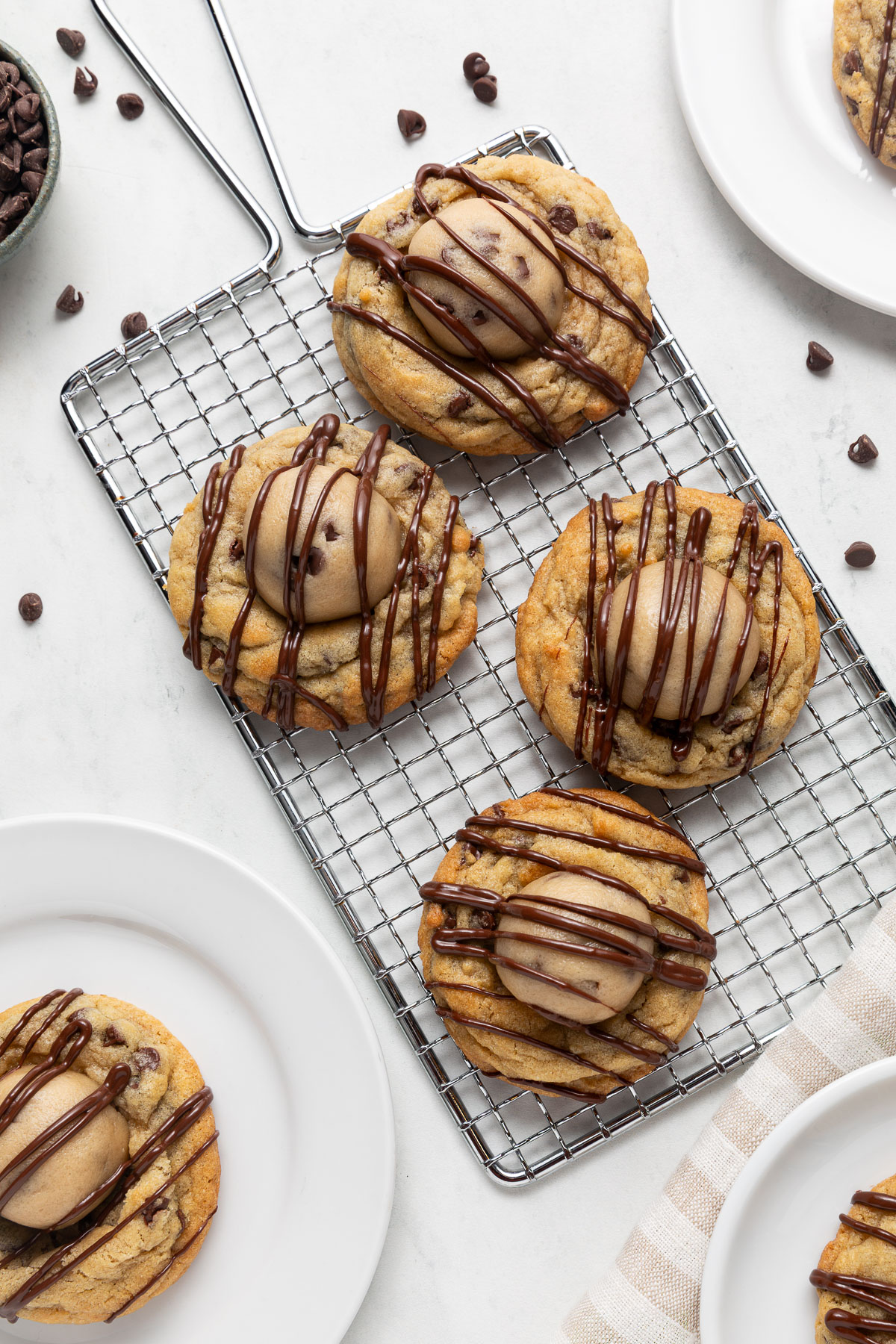 Chocolate chip cookie dough cookies on a wire cooking rack next to plates of cookies and chocolate chips.