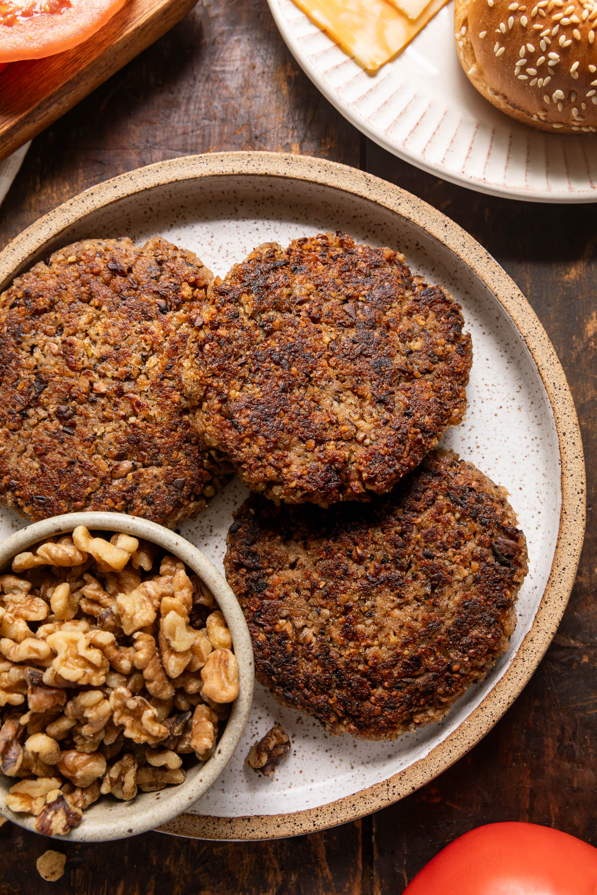 Walnut burger patties on a plate next to a small bowl of walnuts.