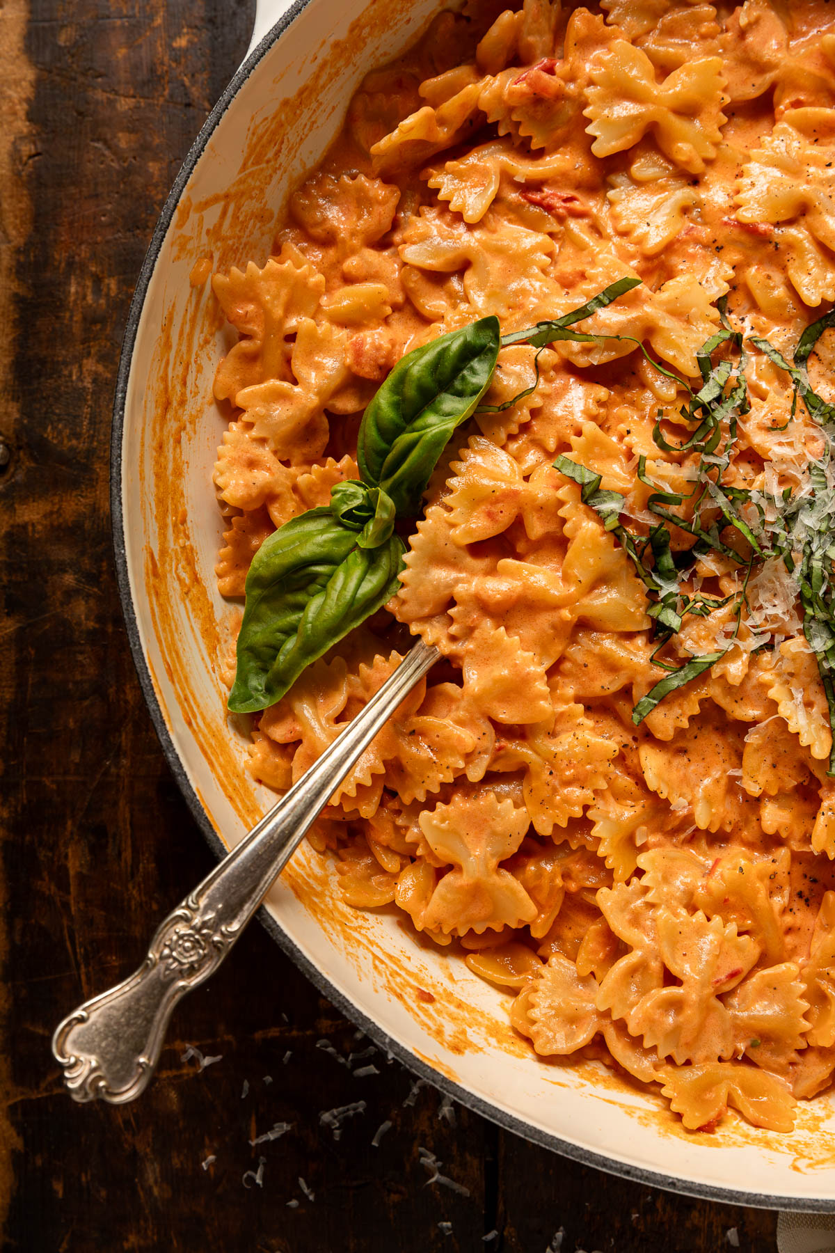 A pot of pasta coated in tomato alfredo sauce topped with fresh basil with a spoon sticking out of it.