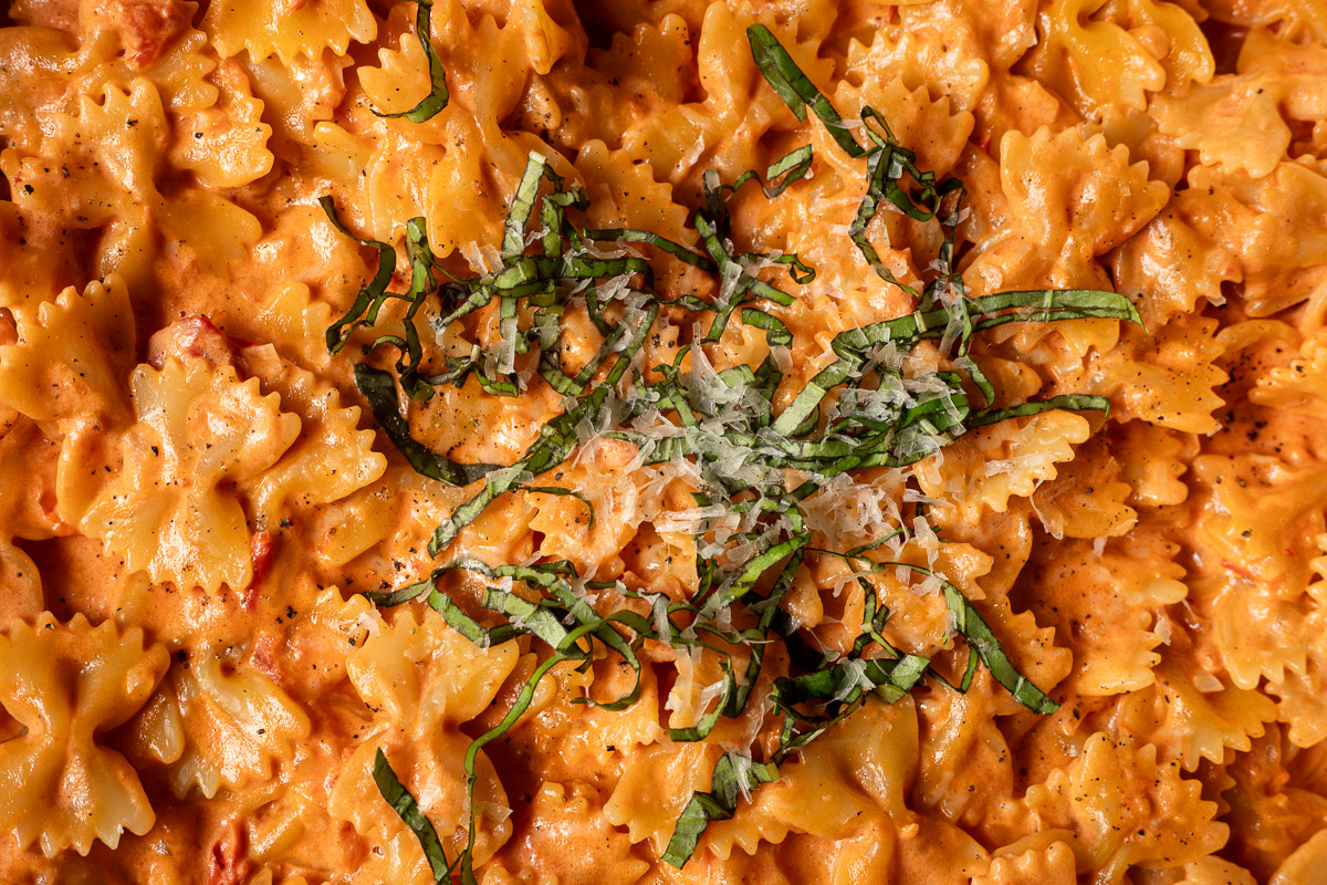 Close up image of tomato alfredo pasta topped with basil and parmesan cheese.