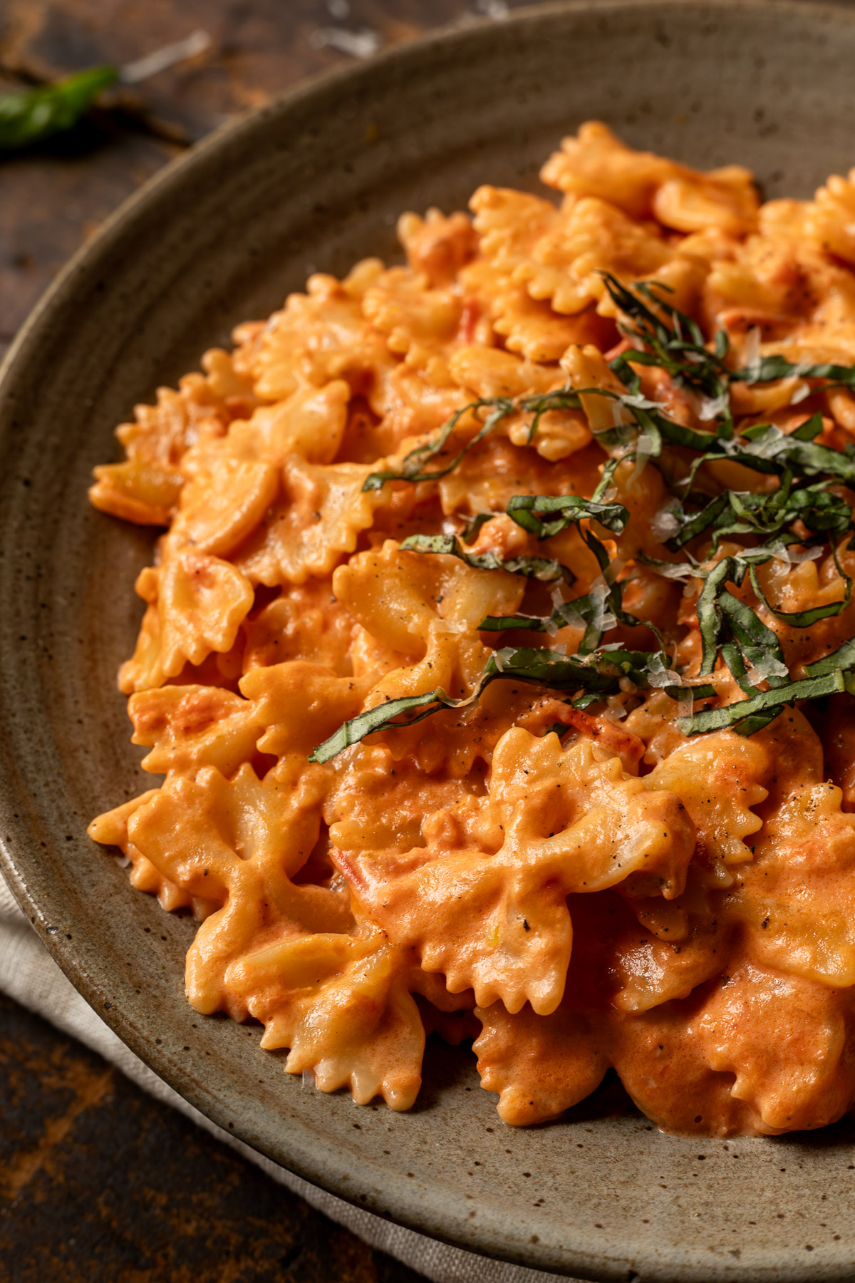 Close up image of tomato alfredo pasta on a plate topped with basil and parmesan cheese.