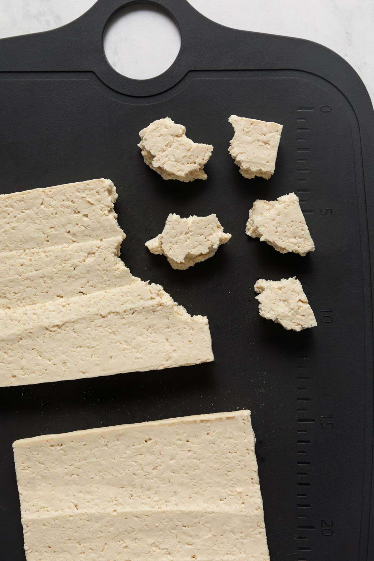 Tofu torn into nuggets on a cutting board.