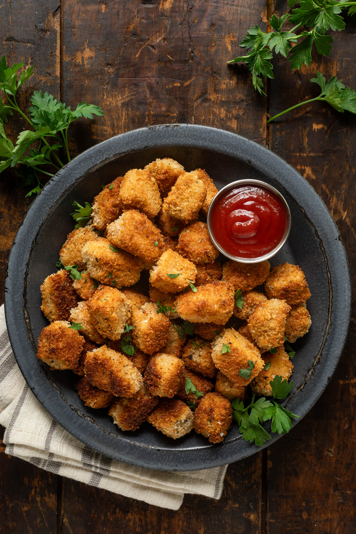 Fried tofu nuggets on a plate garnished with parsley next to a small bowl of ketchup.