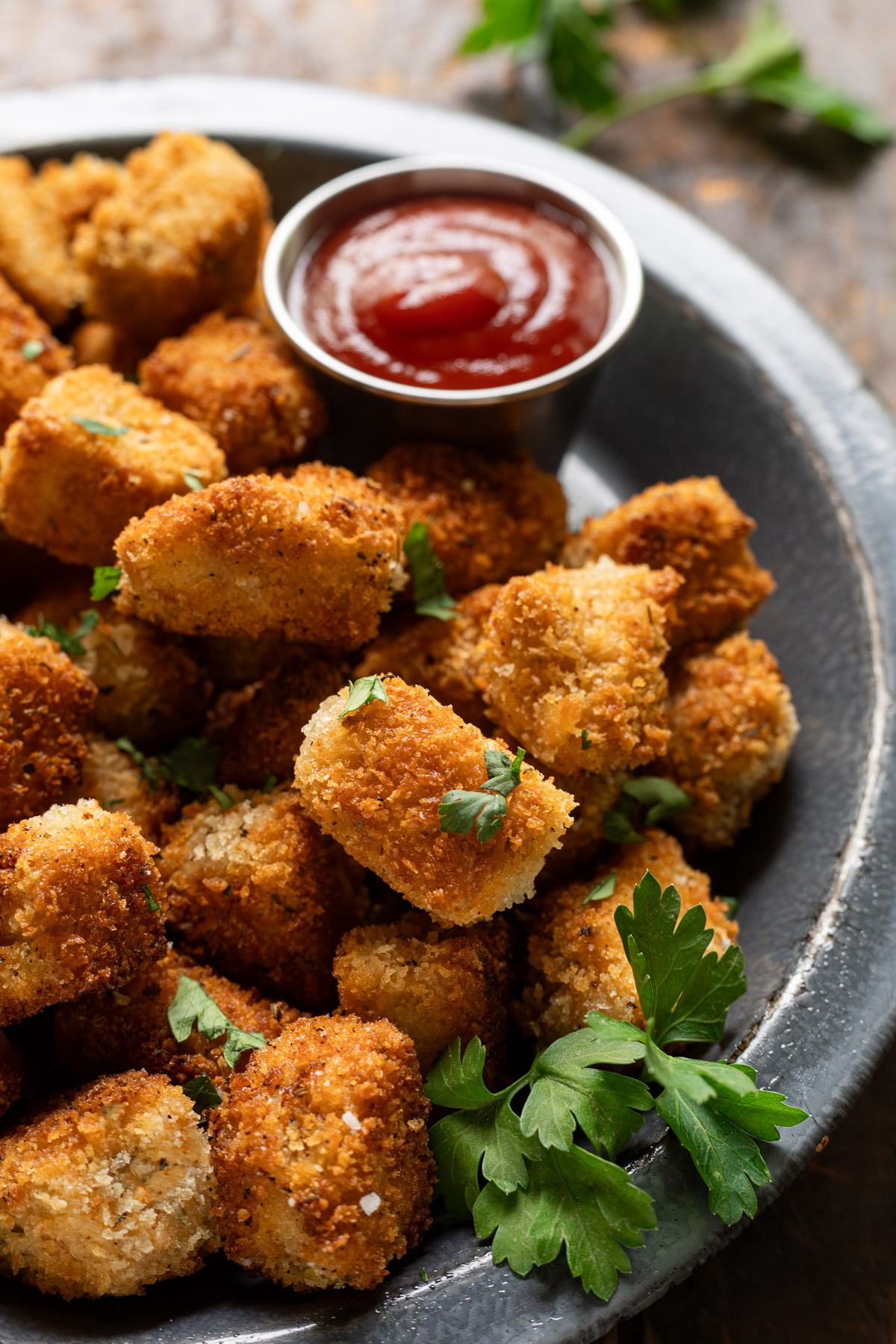 Close up of tofu nuggets on a plate garnished with parsley next to a small bowl of ketchup.