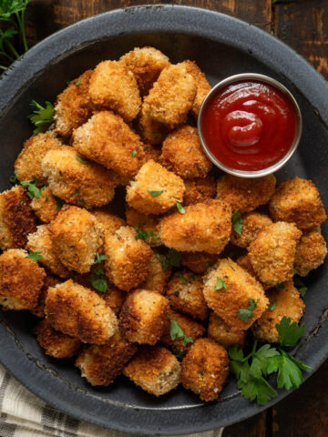 Fried tofu nuggets on a plate garnished with parsley next to a small bowl of ketchup.