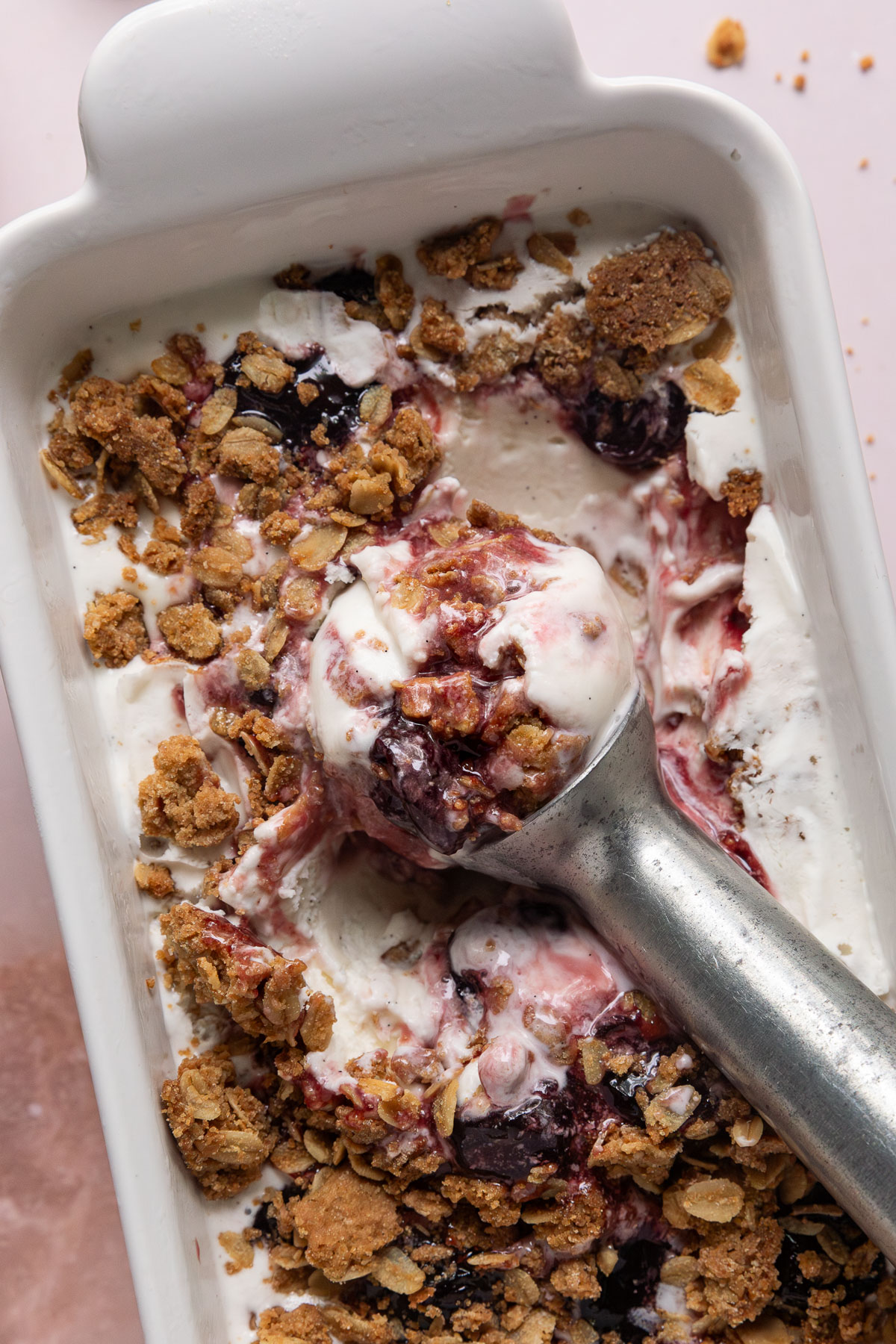 Cherry crisp ice cream in a loaf pan with a ice cream scoop inside it.