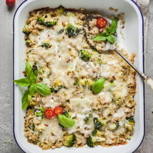 A spoon sticking out of a casserole dish full of broccoli quinoa casserole.