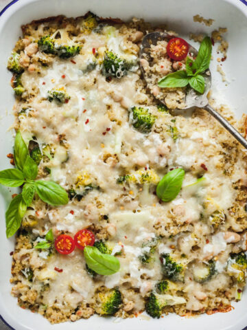 A spoon sticking out of a casserole dish full of broccoli quinoa casserole.