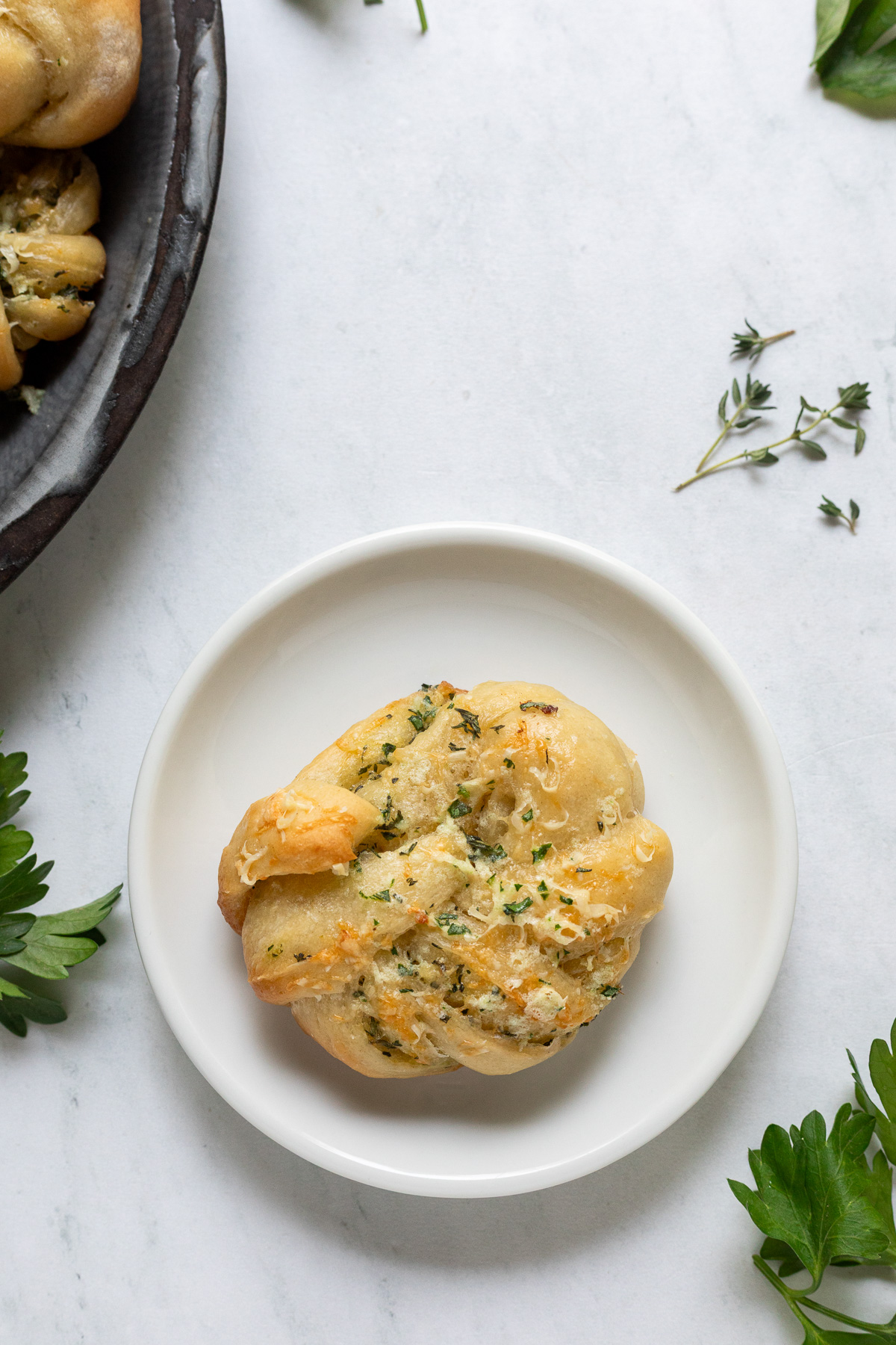A serving platter of garlic parmesan knots next to a small plate with a single garlic knot on it.