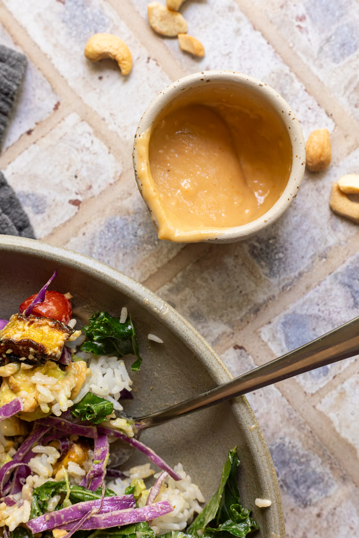 Creamy cashew dressing in a small pouring cup next to a salad.