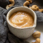 Creamy cashew dressing in a small pouring cup.