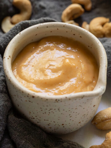 Creamy cashew dressing in a small pouring cup.