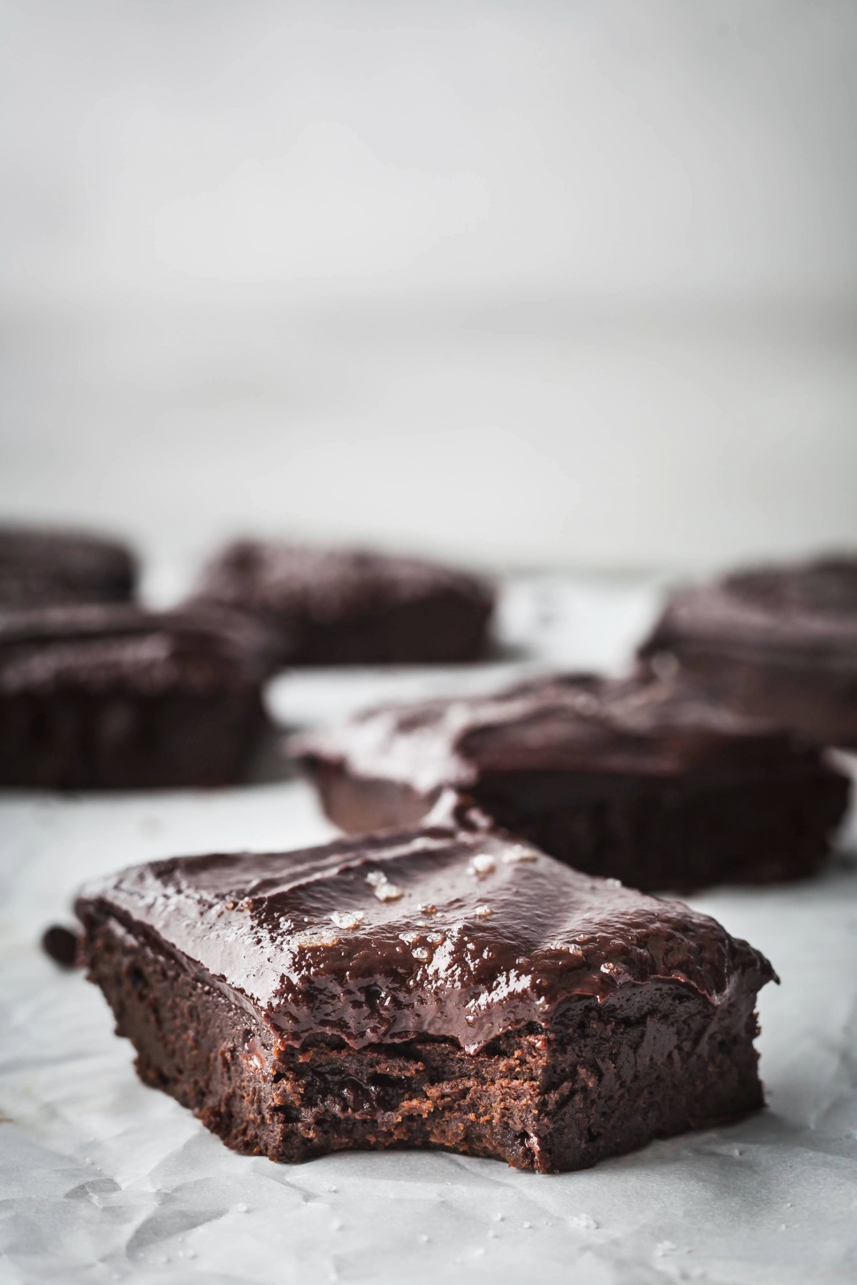 Frosted sweet potato brownies on a sheet of parchment paper, one has a bite taken out of it. 