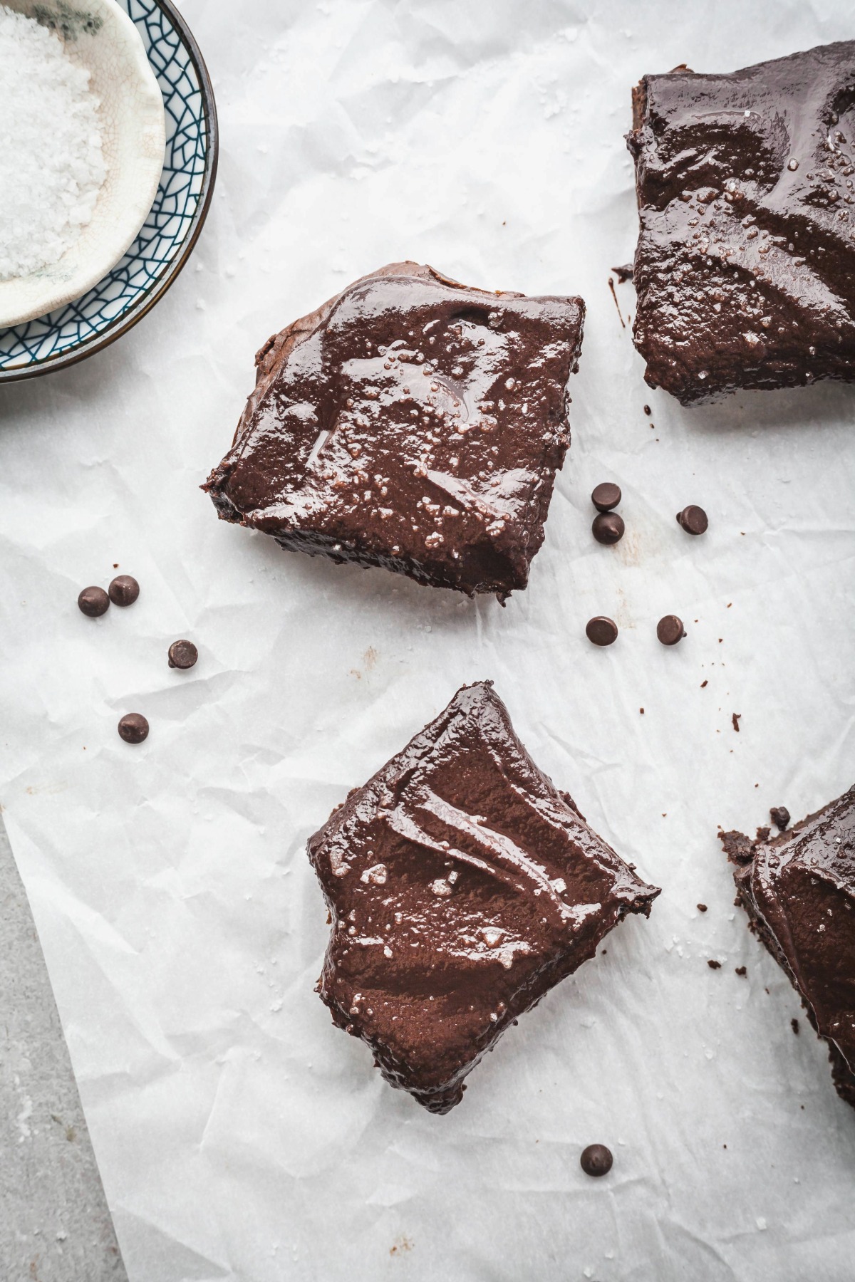 Frosted sweet potato brownies on a sheet of parchment paper, one has a bite taken out of it.