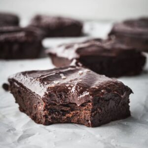 Frosted sweet potato brownies on a sheet of parchment paper, one has a bite taken out of it.