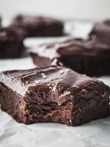Frosted sweet potato brownies on a sheet of parchment paper, one has a bite taken out of it.