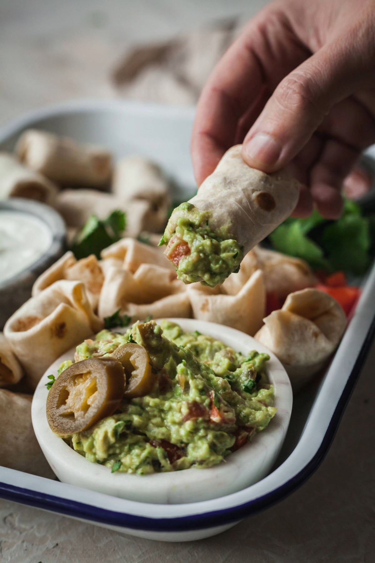 A hand lifting up a vegetarian burrito bite after dipping it in spicy guacamole.