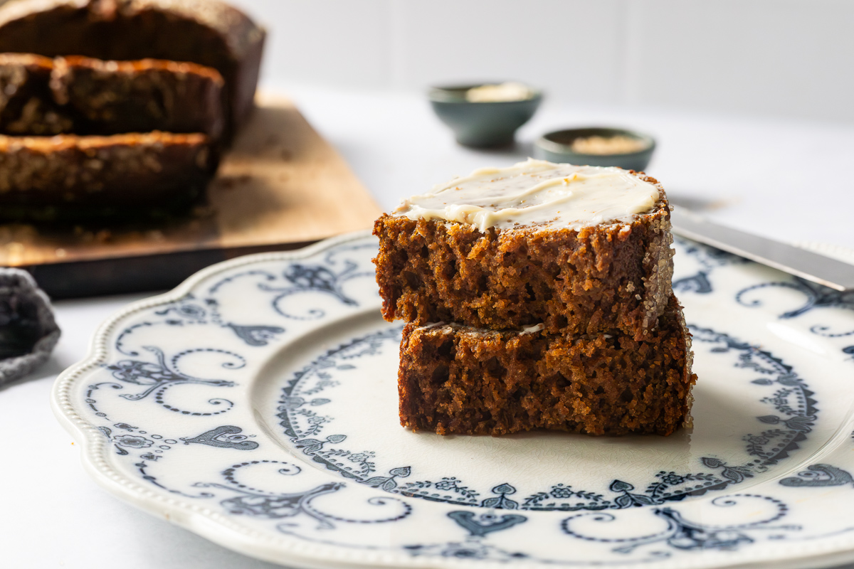A slice of pumpkin gingerbread loaf topped with butter cut in half on a plate.