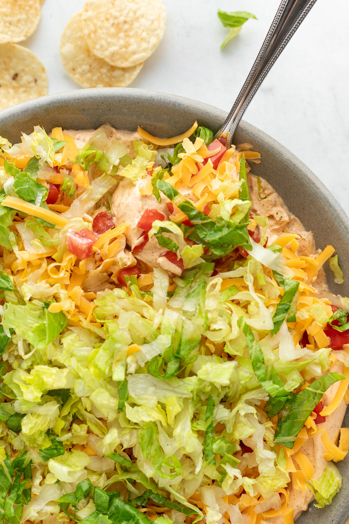 A bowl of taco dip with a spoon sticking out of it.