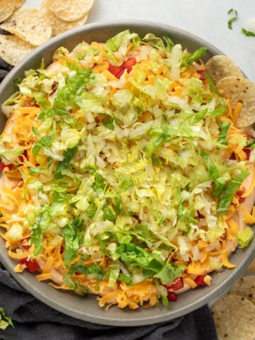 A bowl of taco dip with a chip sticking out of it.