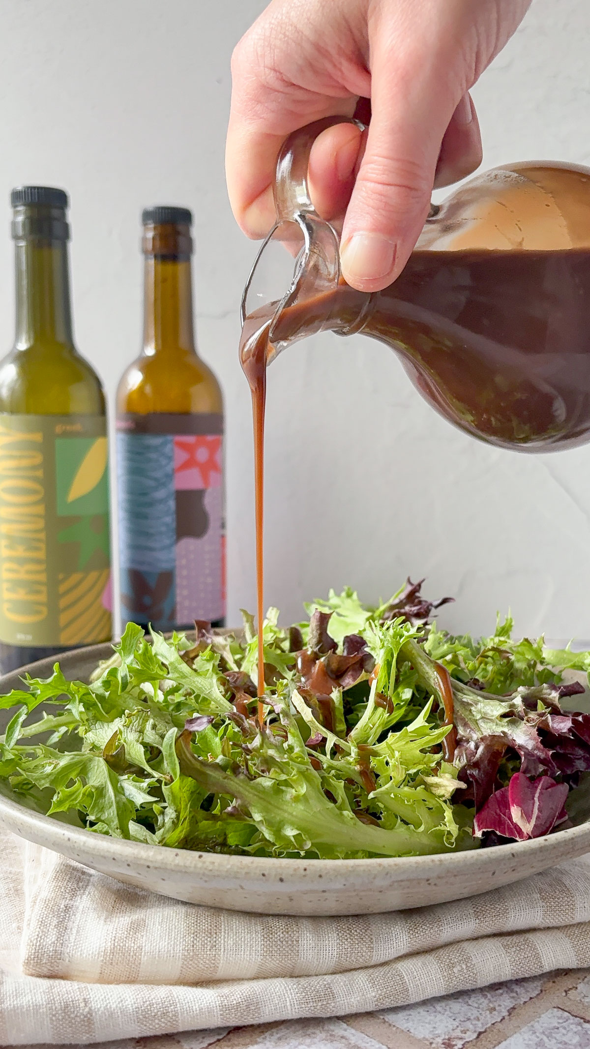 A glass jug full of balsamic vinaigrette being drizzled on a salad.