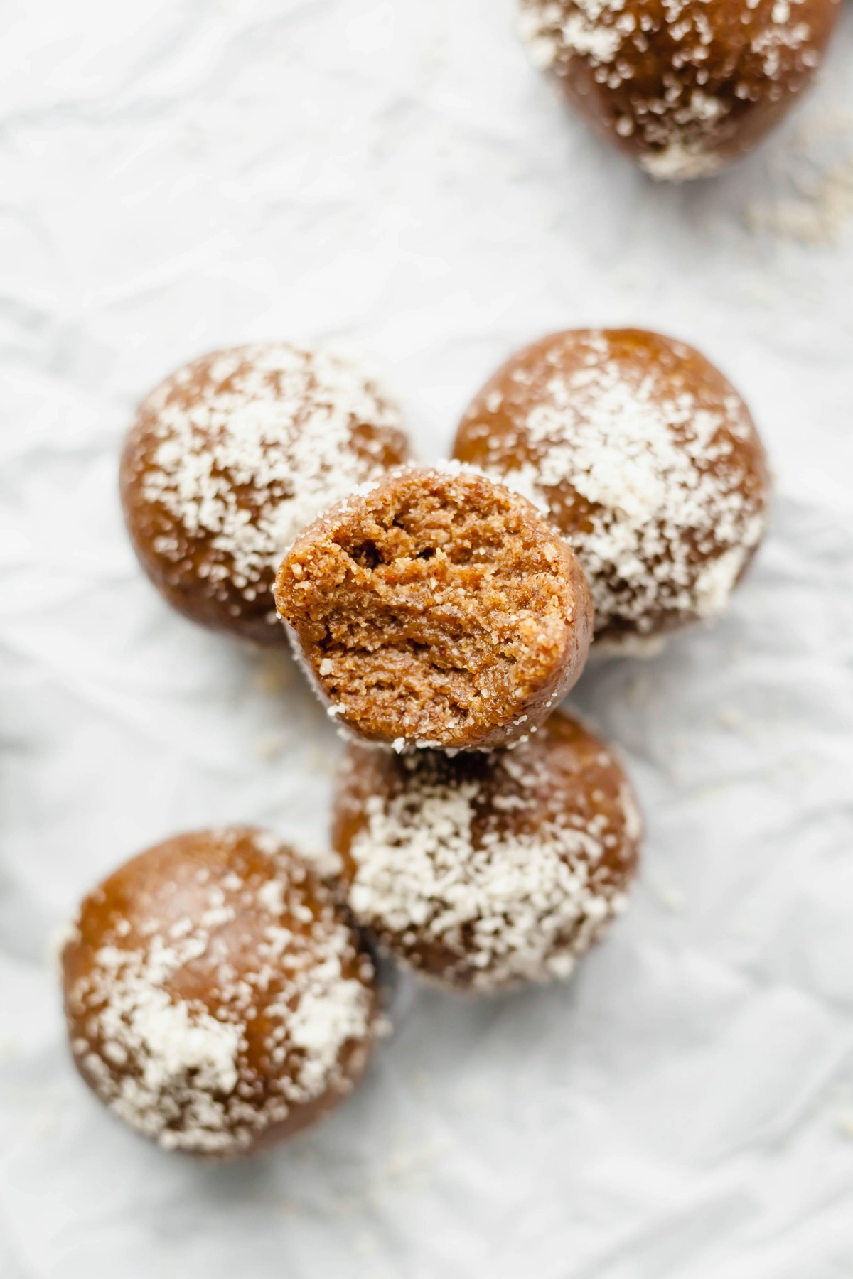 A pile of gingerbread energy balls sheet of parchment paper, the ball on top has a bite taken out of it.