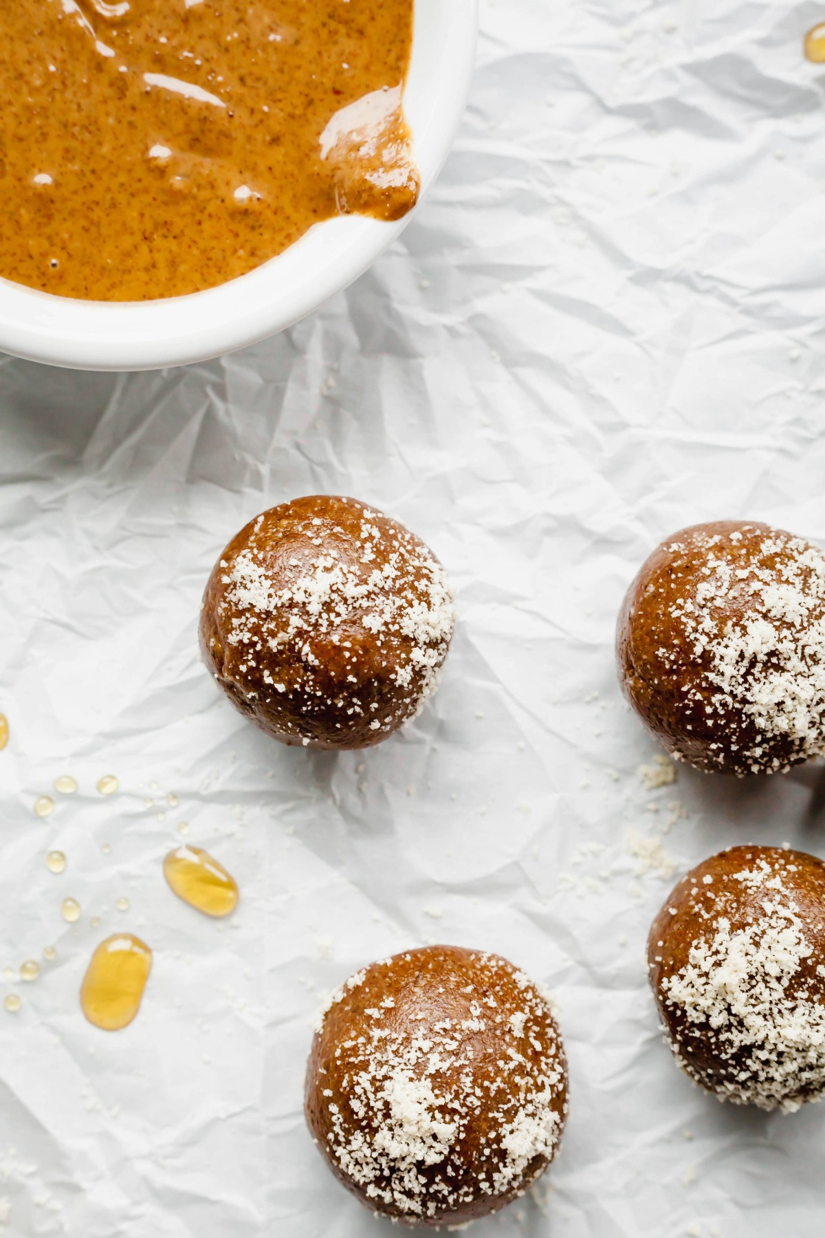 A pile of gingerbread energy balls sheet of parchment paper next to a bowl of almond butter.