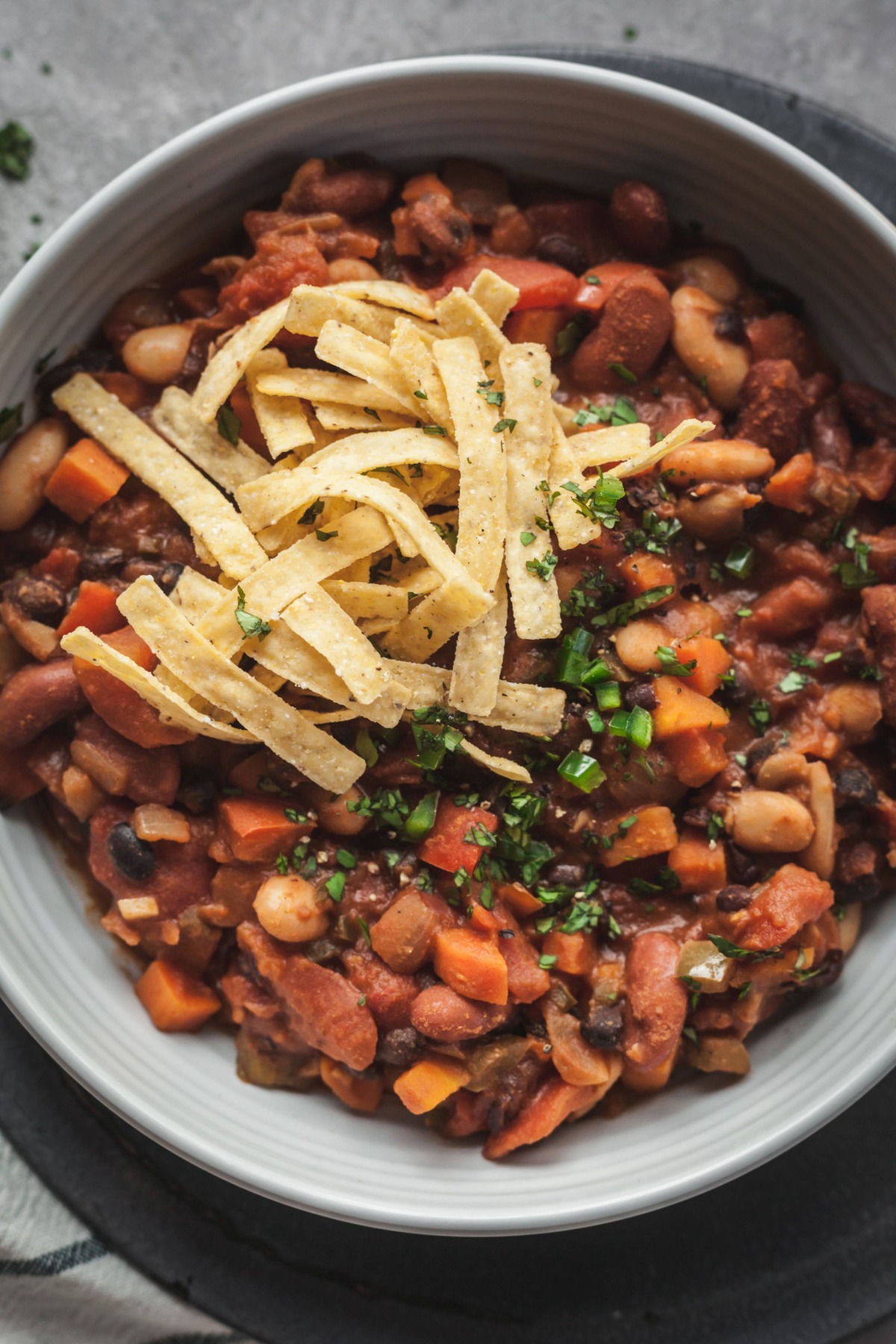 A bowl of vegetarian chili topped with tortilla strips and fresh chives.