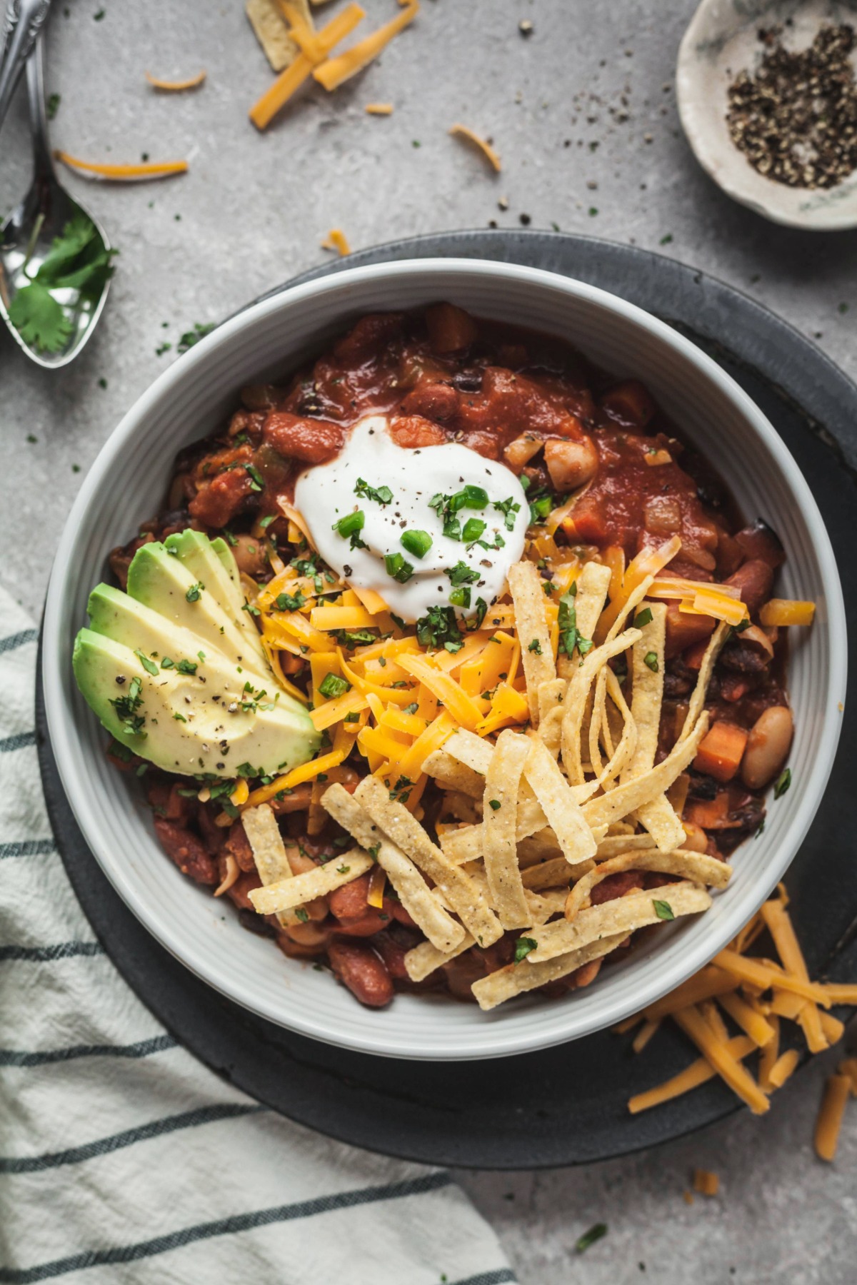 A bowl of vegetarian chili topped with sour cream, tortilla strips, sliced avocado, and fresh chives. 