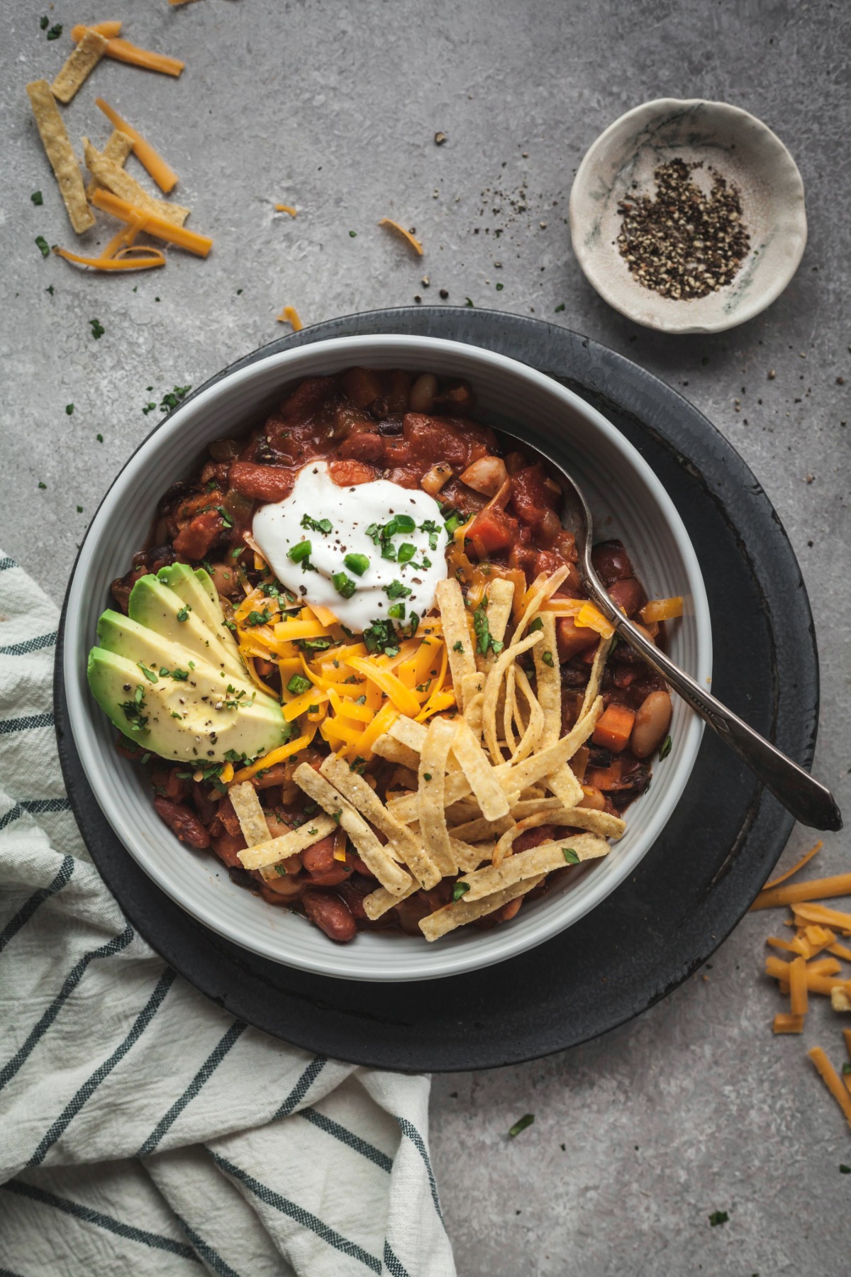 A bowl of vegetarian chili topped with sour cream, tortilla strips, sliced avocado, and fresh chives.