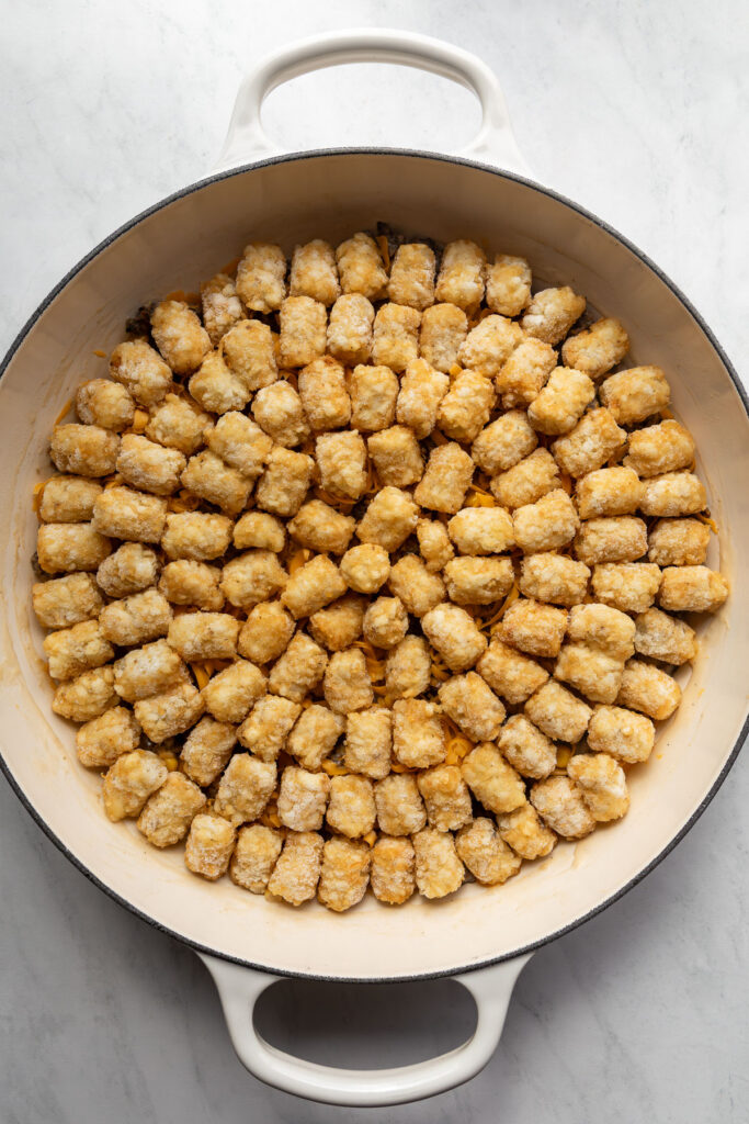 Uncooked tater tot casserole in a braiser.