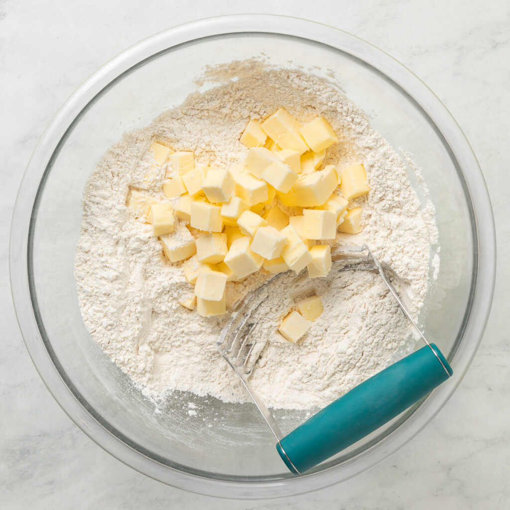 a pastry cutter in a large bowl with cubed butter and dry ingredients for a homemade pie crust.