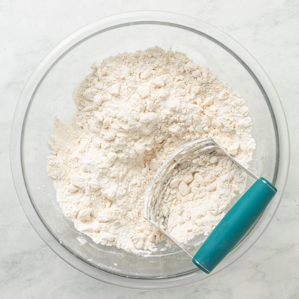 a large bowl and pastry cutter with the butter cut into the dry ingredients for pie crust.