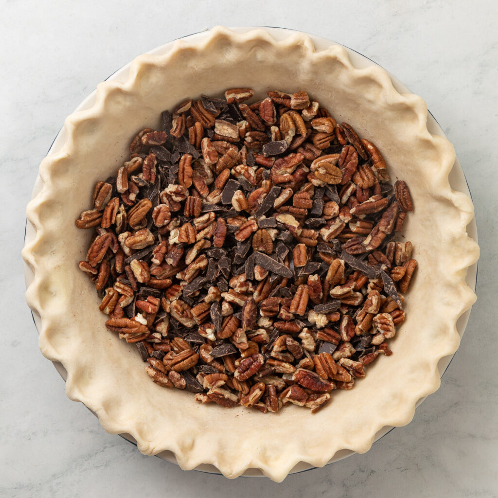 chopped pecans and dark chocolate in the bottom of a pie shell.