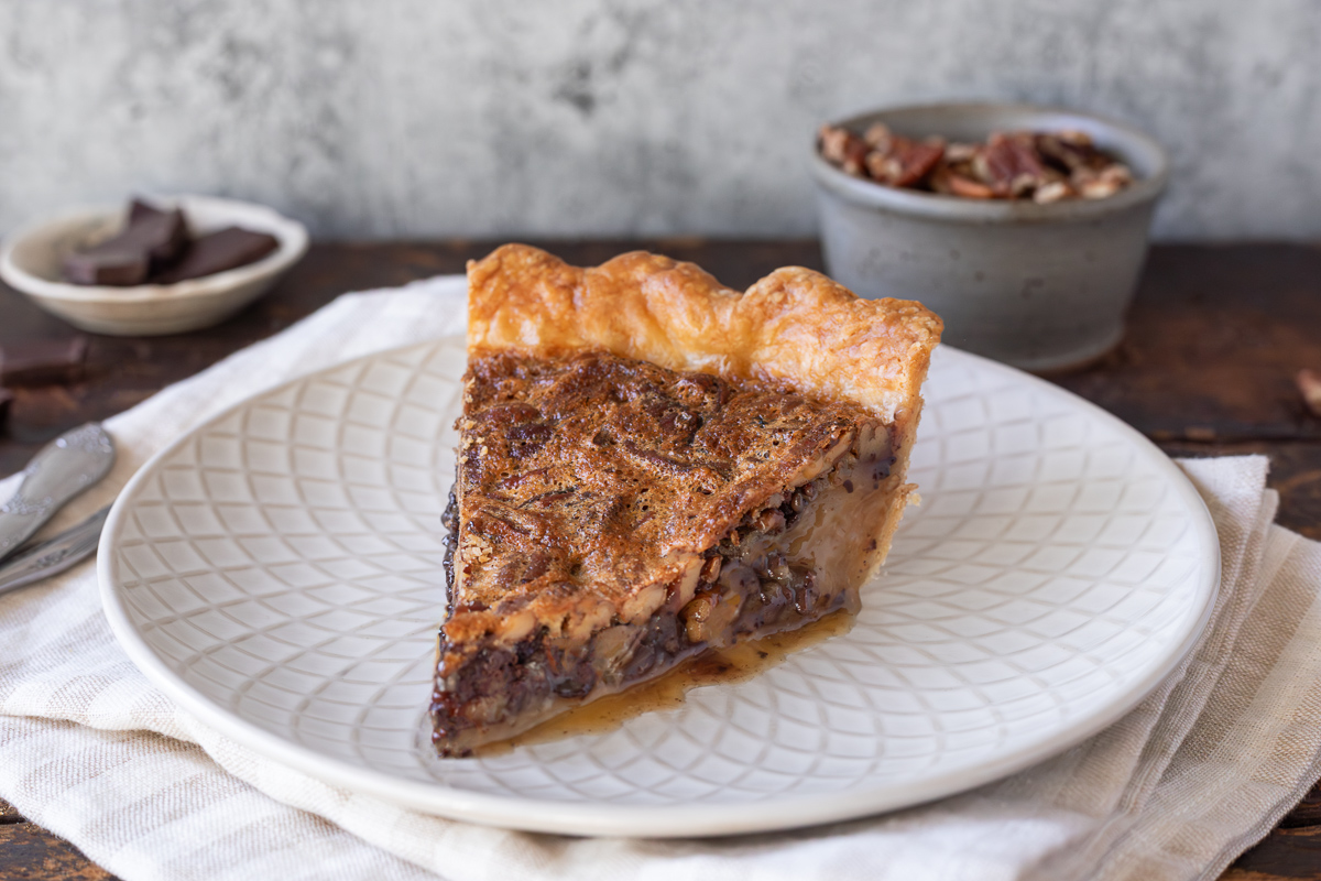 a slice of chocolate bourbon pecan pie on a small plate.
