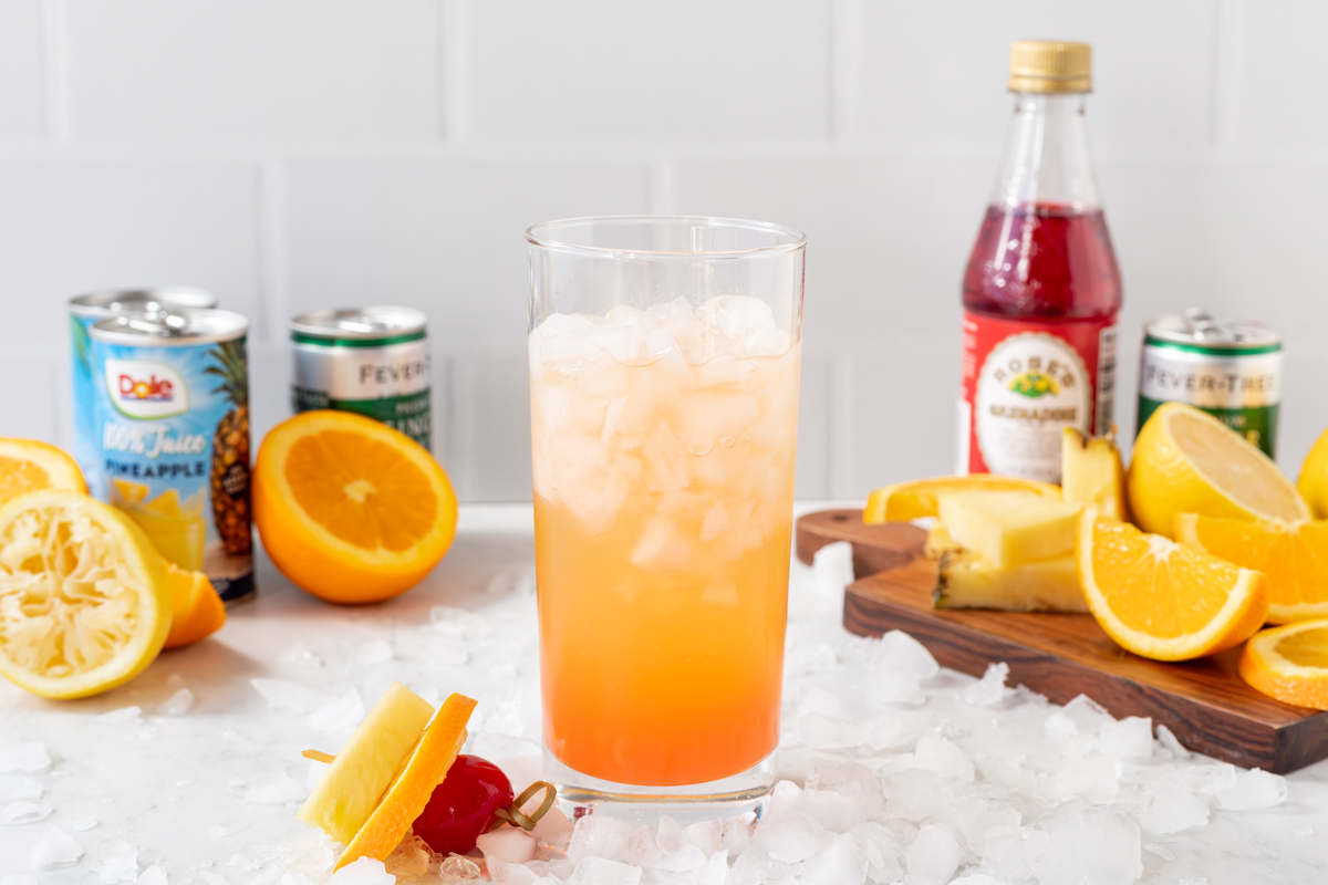 Cinderella mocktail in a glass surrounded by crushed ice, in the background you can see all the ingredients that go into the drink.