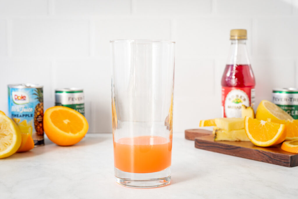 Juice mixture in a glass. In the background there is all the ingredients used to make a cinderella mocktail.