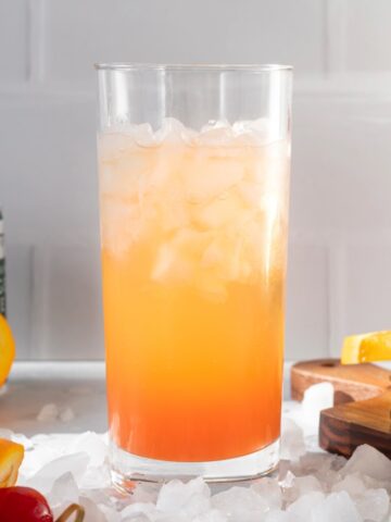 Cinderella mocktail in a glass surrounded by crushed ice, in the background you can see all the ingredients that go into the drink.