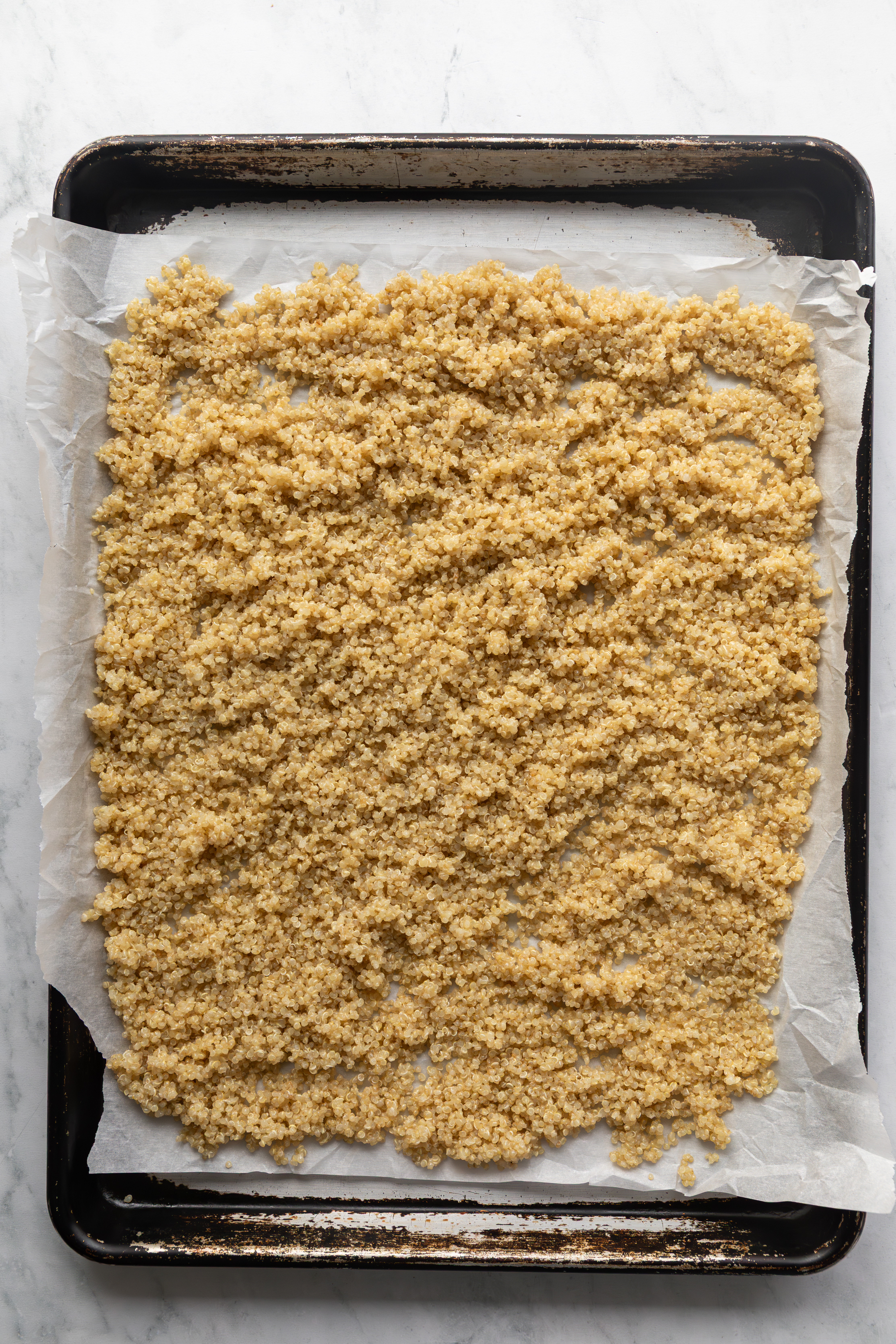 Quinoa spread out on a baking sheet lined with parchment paper.