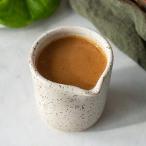 Peanut dressing in a small ceramic cup with a spout.