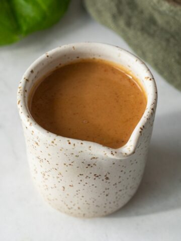 Peanut dressing in a small ceramic cup with a spout.