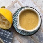 Lemon tahini dressing in a ceramic bowl next to a squeezed lemon half.
