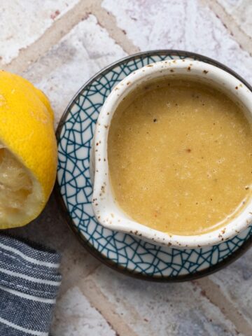 Lemon tahini dressing in a ceramic bowl next to a squeezed lemon half.